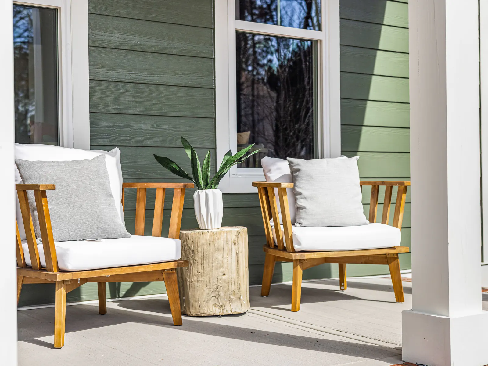Two wooden armchairs with white cushions on a covered front porch